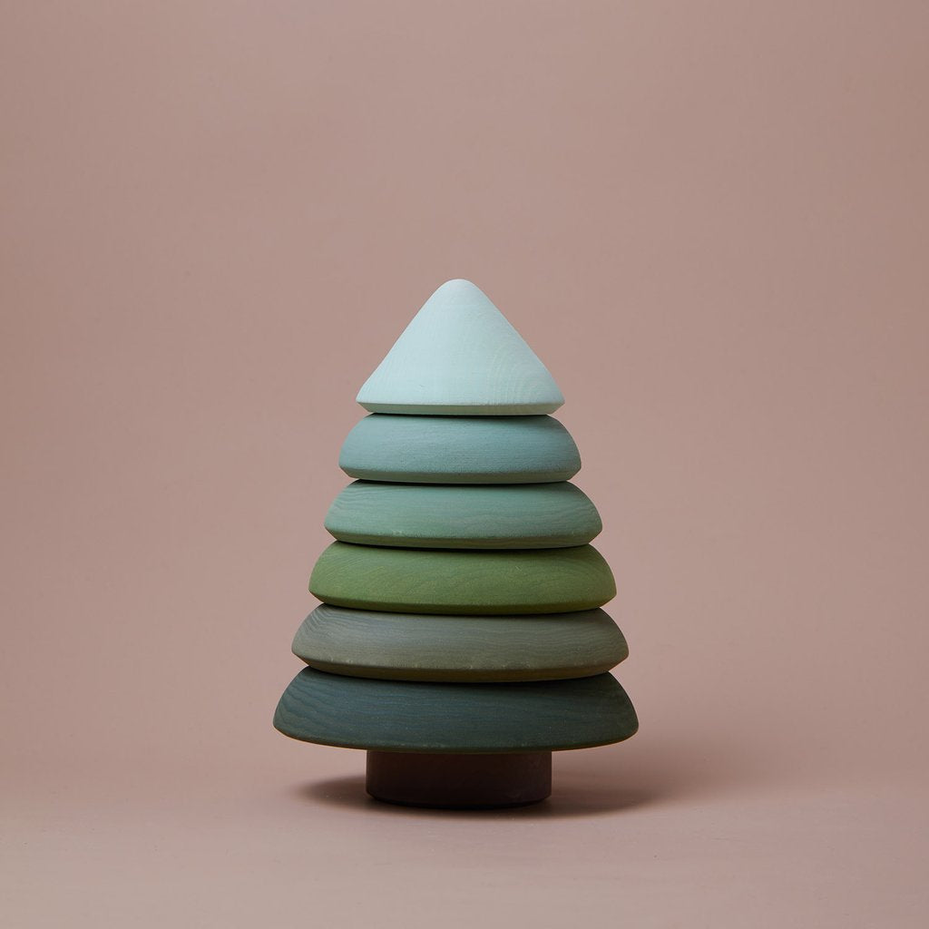 A minimalist, handmade wooden tree figurine with seven stacked, differently colored layers transitions from white at the top to dark green at the bottom, set against a light brown background. Crafted using non-toxic paint, it exemplifies sustainable responsibility. This is the Raduga Grez | Fir Tree Stacker.