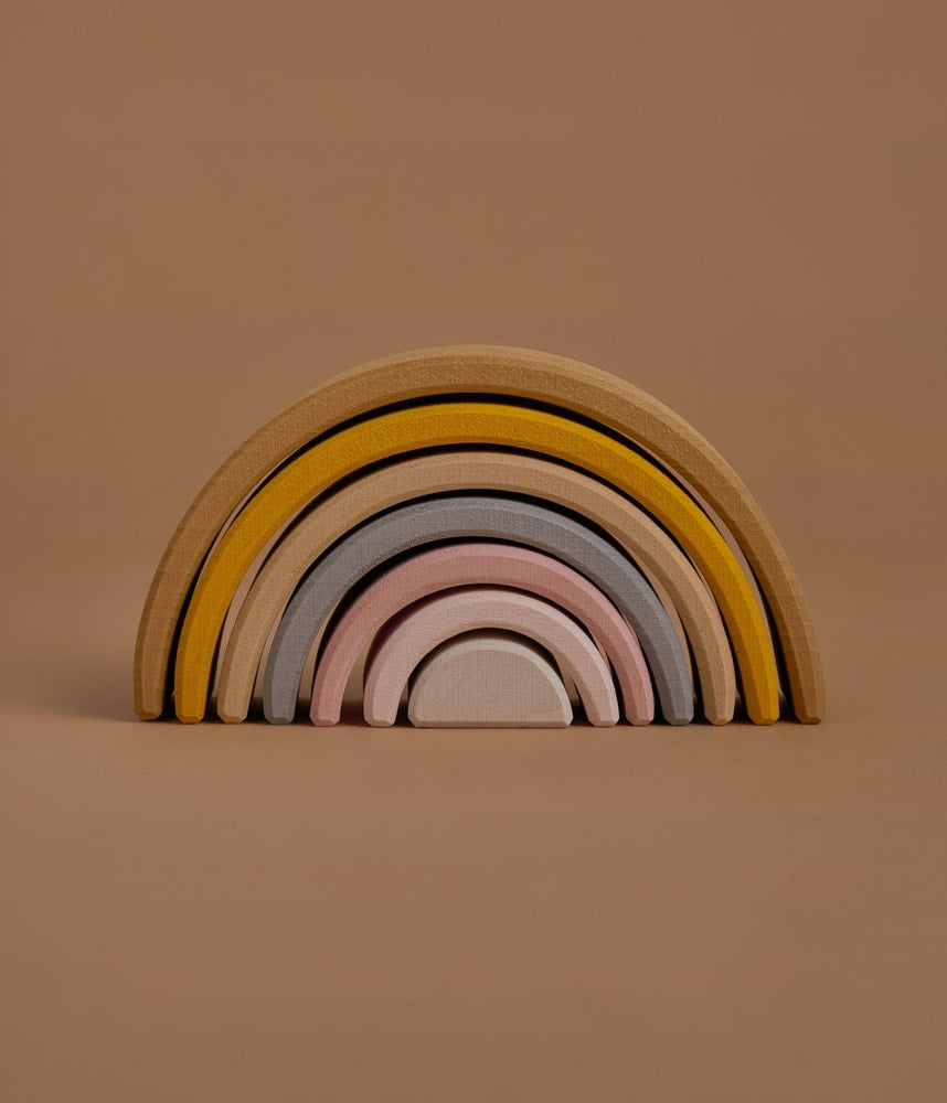 A stacking toy with 7 pastel tone wooden arcs stacked into a rainbow shape. 