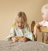 A kid playing with a stacking toy with 7 pastel tone wooden arcs stacked into a rainbow shape. 