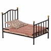 A Maileg Miniature Bed with decorative golden knobs, featuring a textured pink bedspread and a floral pillow, isolated on a white background.