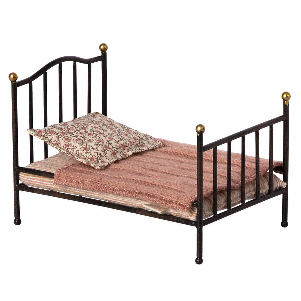 A Maileg Miniature Bed with decorative golden knobs, featuring a textured pink bedspread and a floral pillow, isolated on a white background.