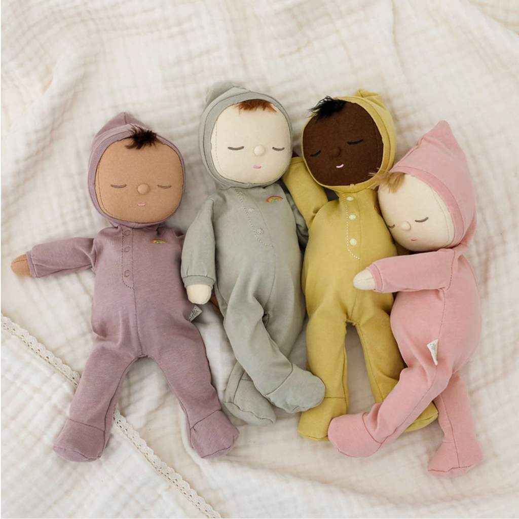 Four soft dolls with different skin tones in pajamas under a gauze blanket. 