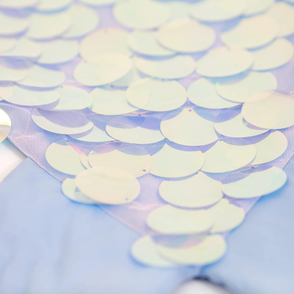 A close-up image of numerous translucent, iridescent sequins scattered over a light blue fabric surface, reflecting soft pastel colors from the Meri Meri Mermaid Wrap Costume - Final Sale.